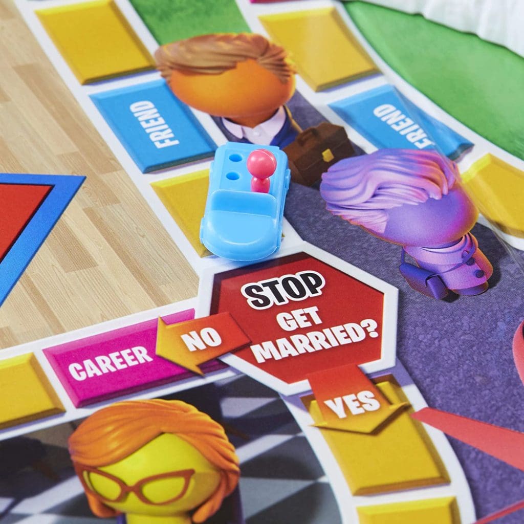 Game of Life 2021 'Your Life Your Way' in a lifestyle photoshoot with a close up on a blue car with multi color pegs. Made by Hasbro Gaming