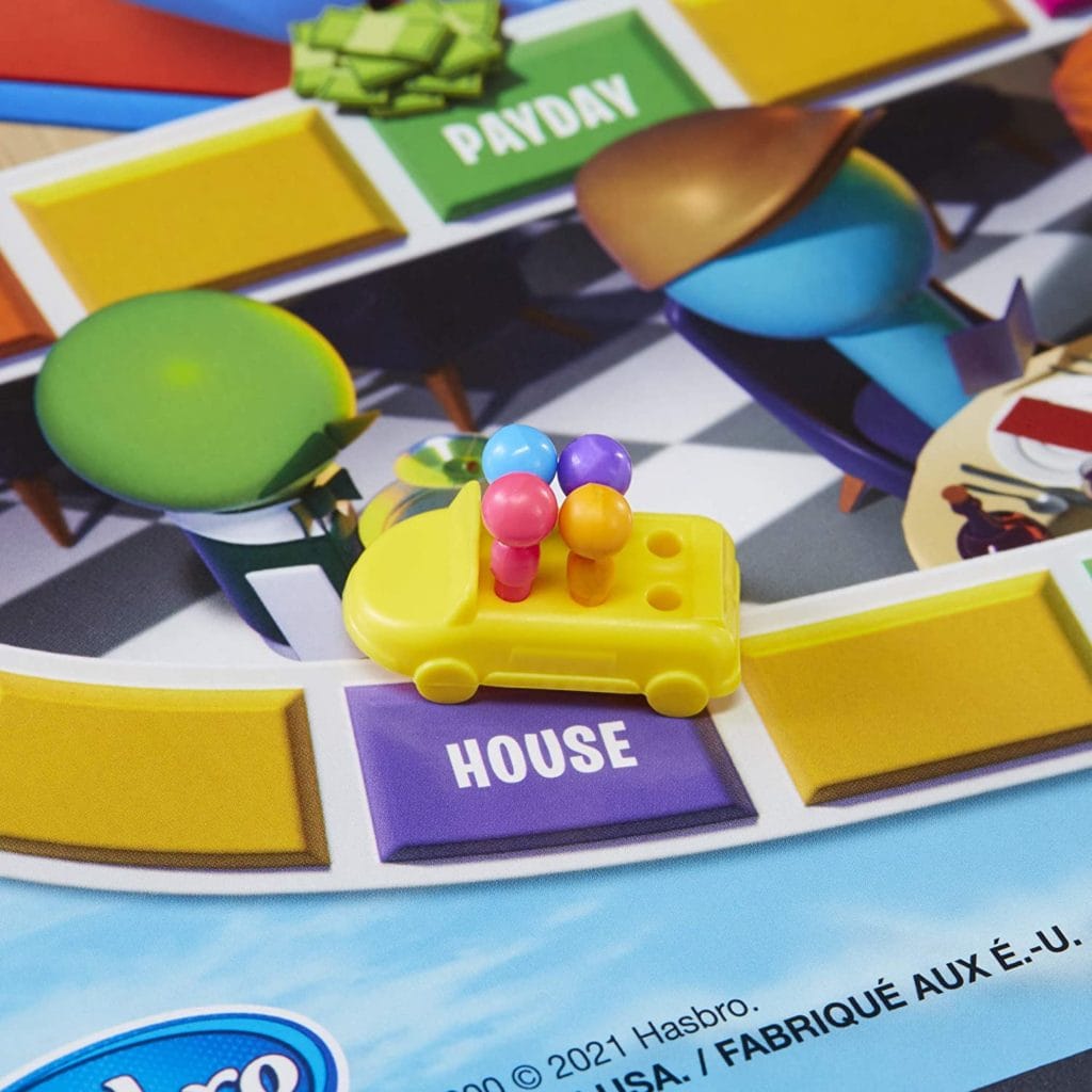 Game of Life 2021 'Your Life Your Way' in a lifestyle photoshoot with a close up on a yellow car with 4 multi color pegs. Made by Hasbro Gaming