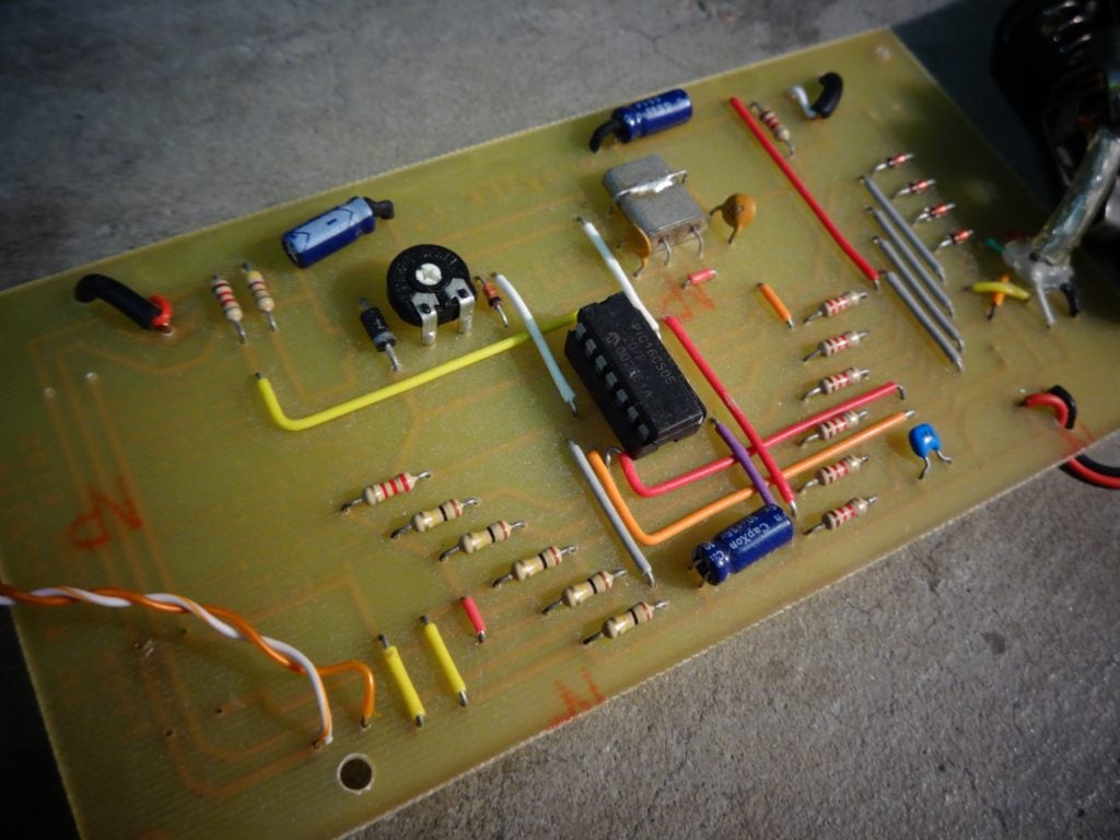 Gray Bright circuit board with smily face of components that is a PONG game in a circuit board with battery holder and buttons close up of components