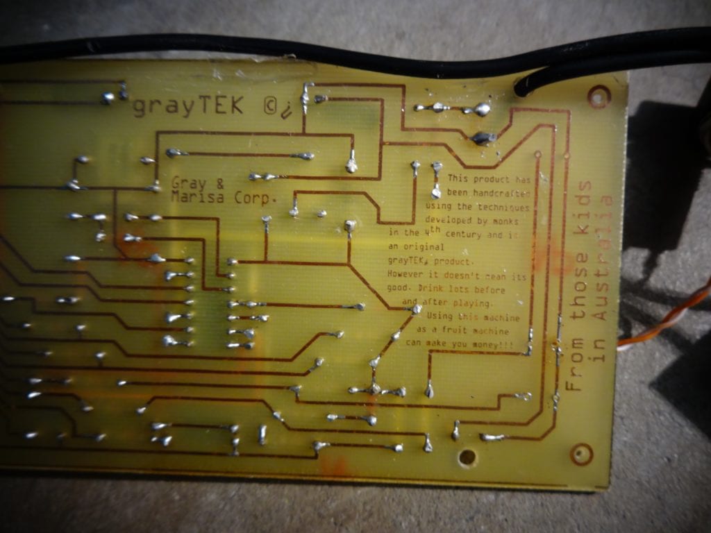 Gray Bright circuit board with smily face of components that is a PONG game in a circuit board with battery holder and buttons close up of components back of PCB on the right side